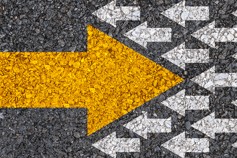 A painted concrete ground displays one large yellow arrow disrupts the flow of oncoming smaller white arrows.