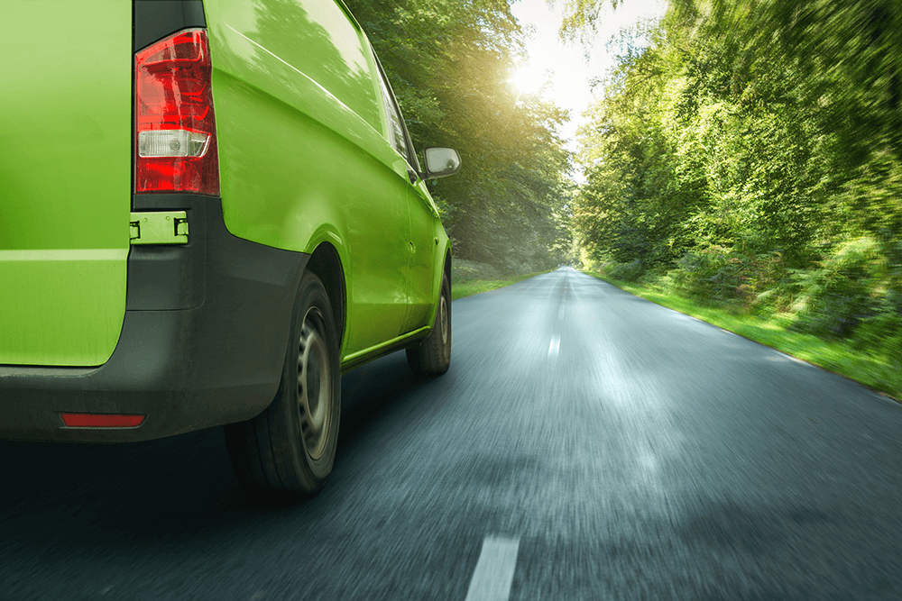 A green delivery van courier vehicle drives on a highway through a green forest