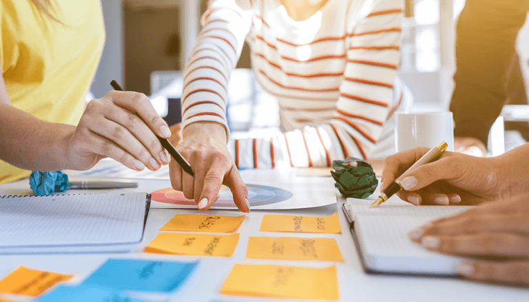 Professionals sit around a table, pointing at and writing on colorful sticky notes